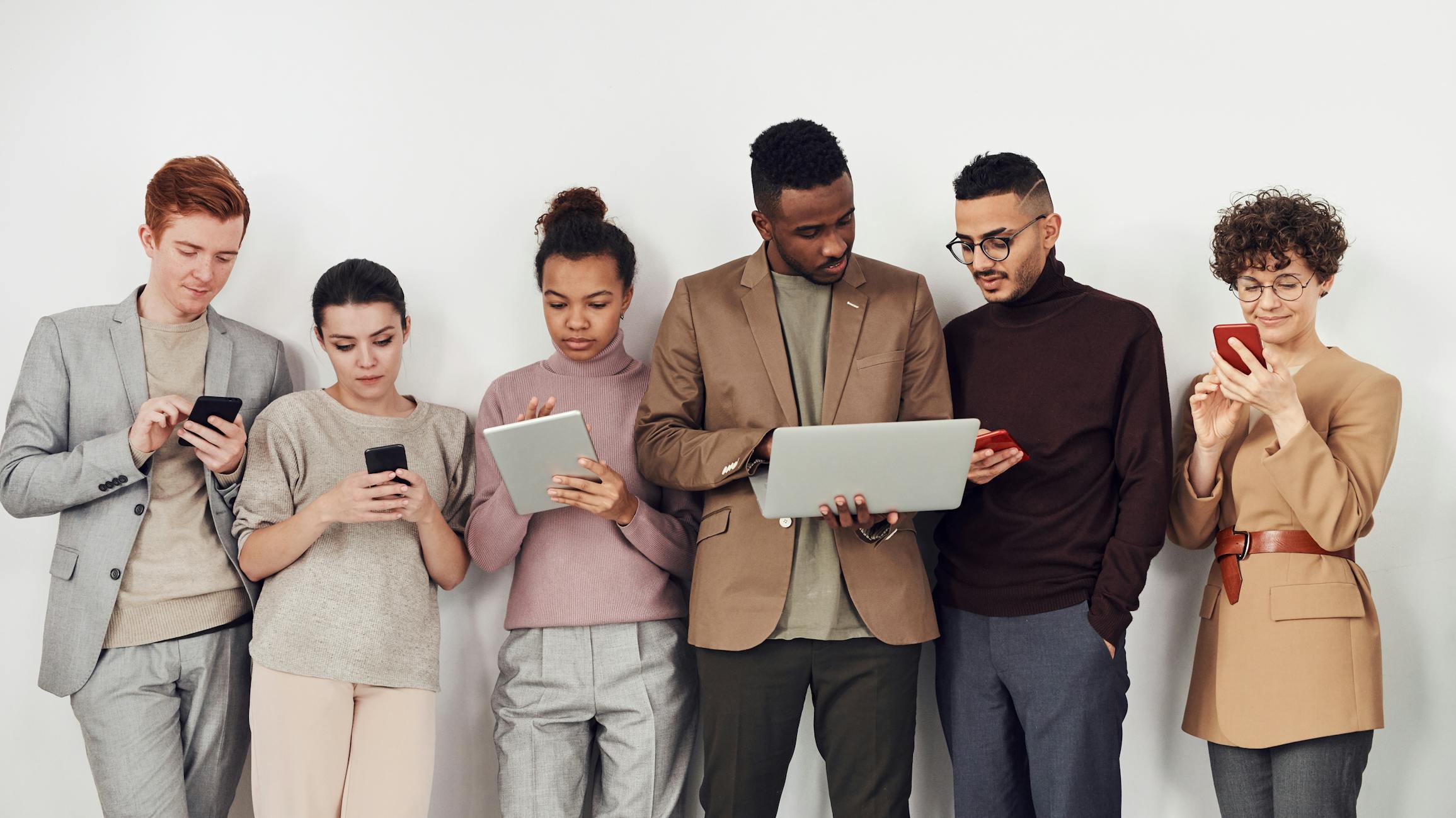 A diverse group of young professionals using smartphones, tablets, and laptops — the people who use modern community platforms.